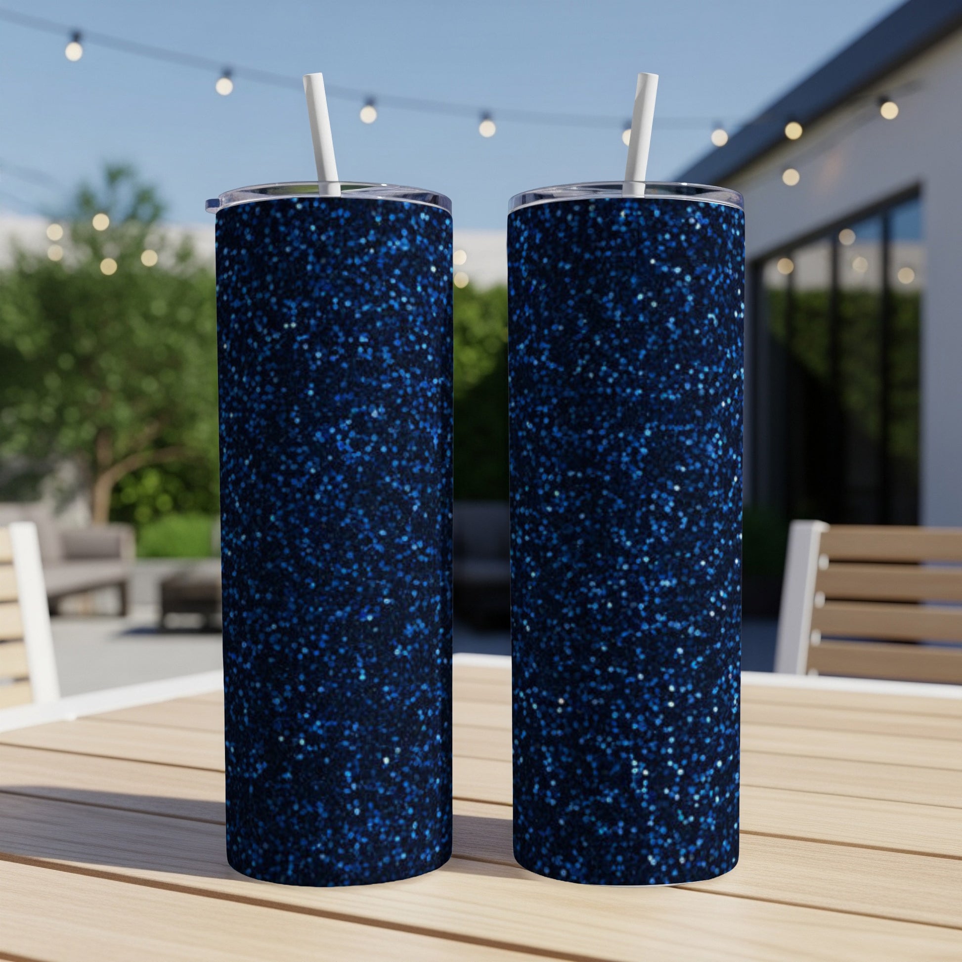 Two tall, sparkly navy blue glitter tumblers with white straws on a table.