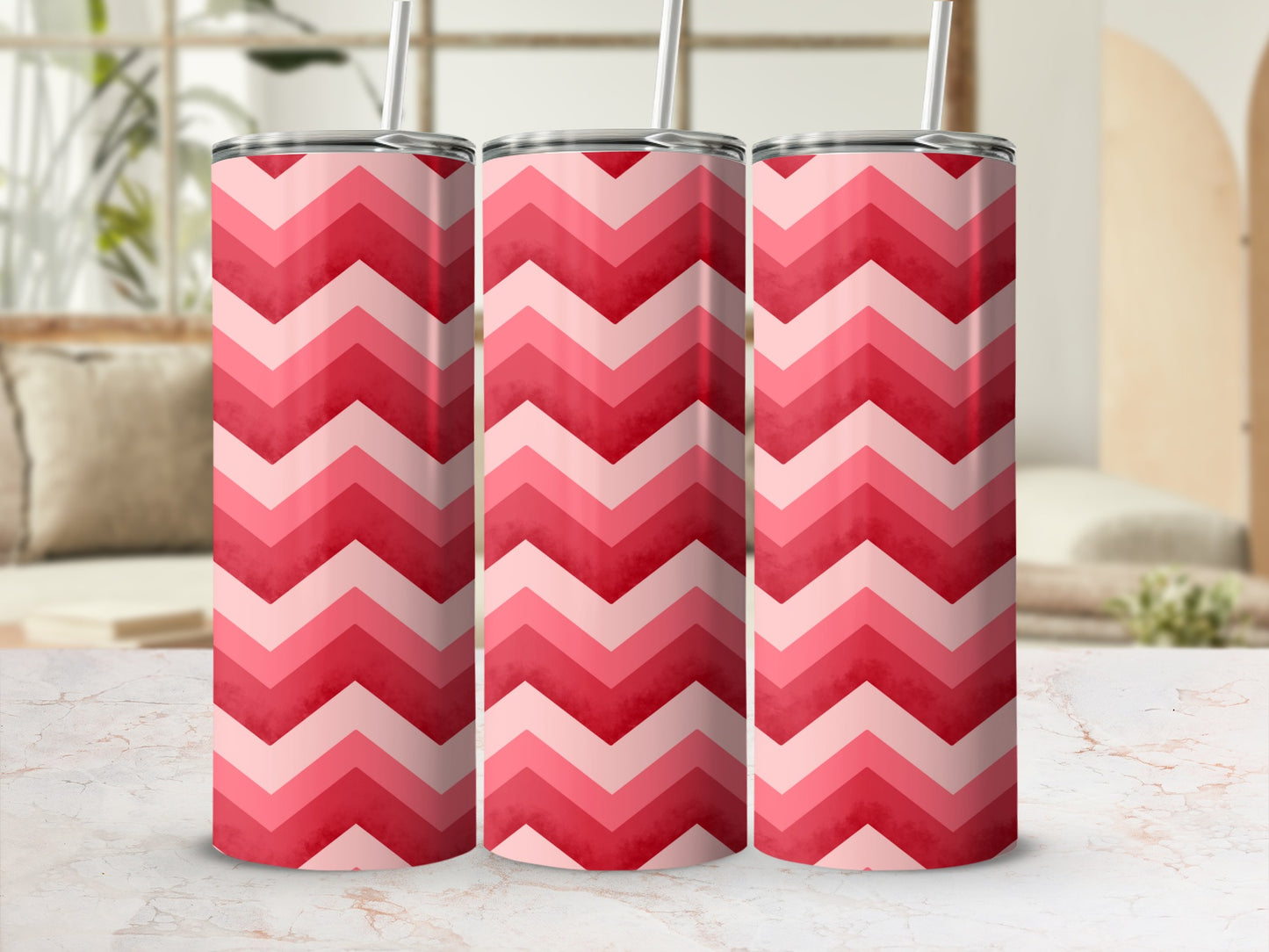 Three pink chevron pattern tumblers with straws on a white table.