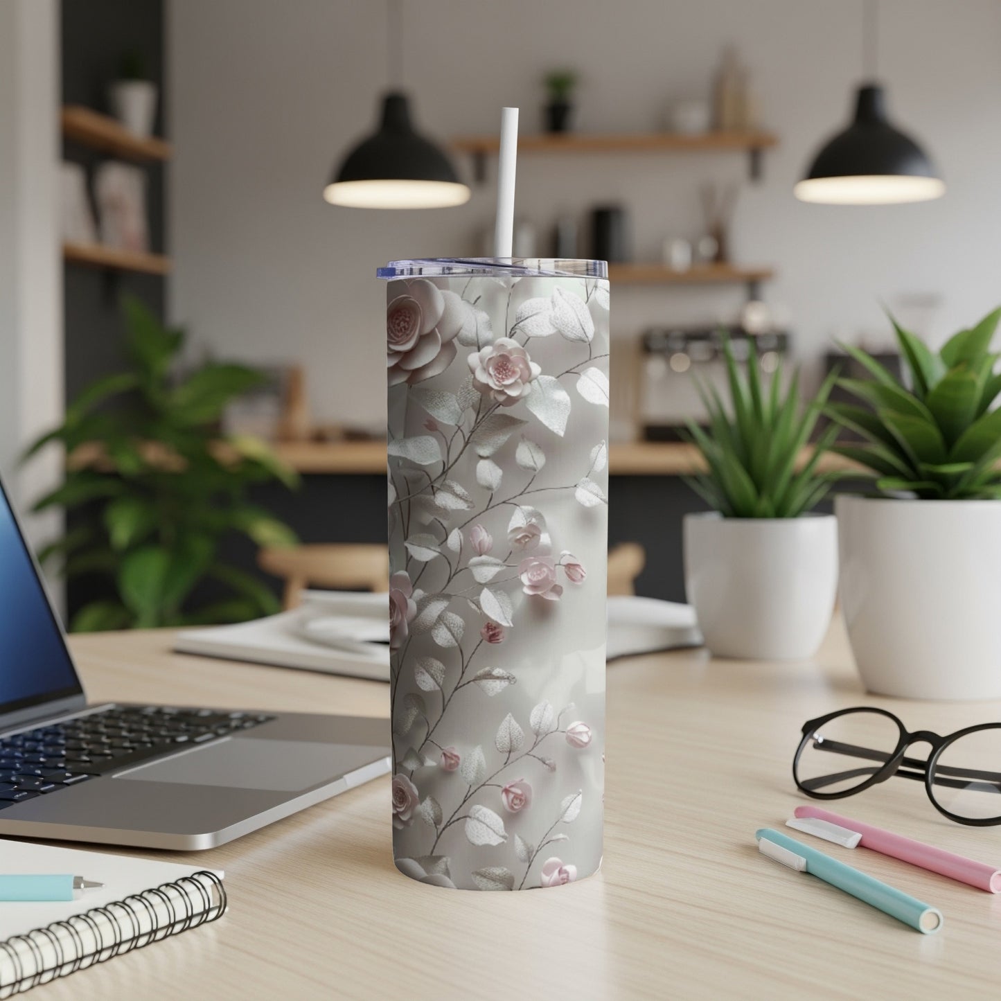 Silver tumbler with a floral pattern, resting on a desk with a laptop.