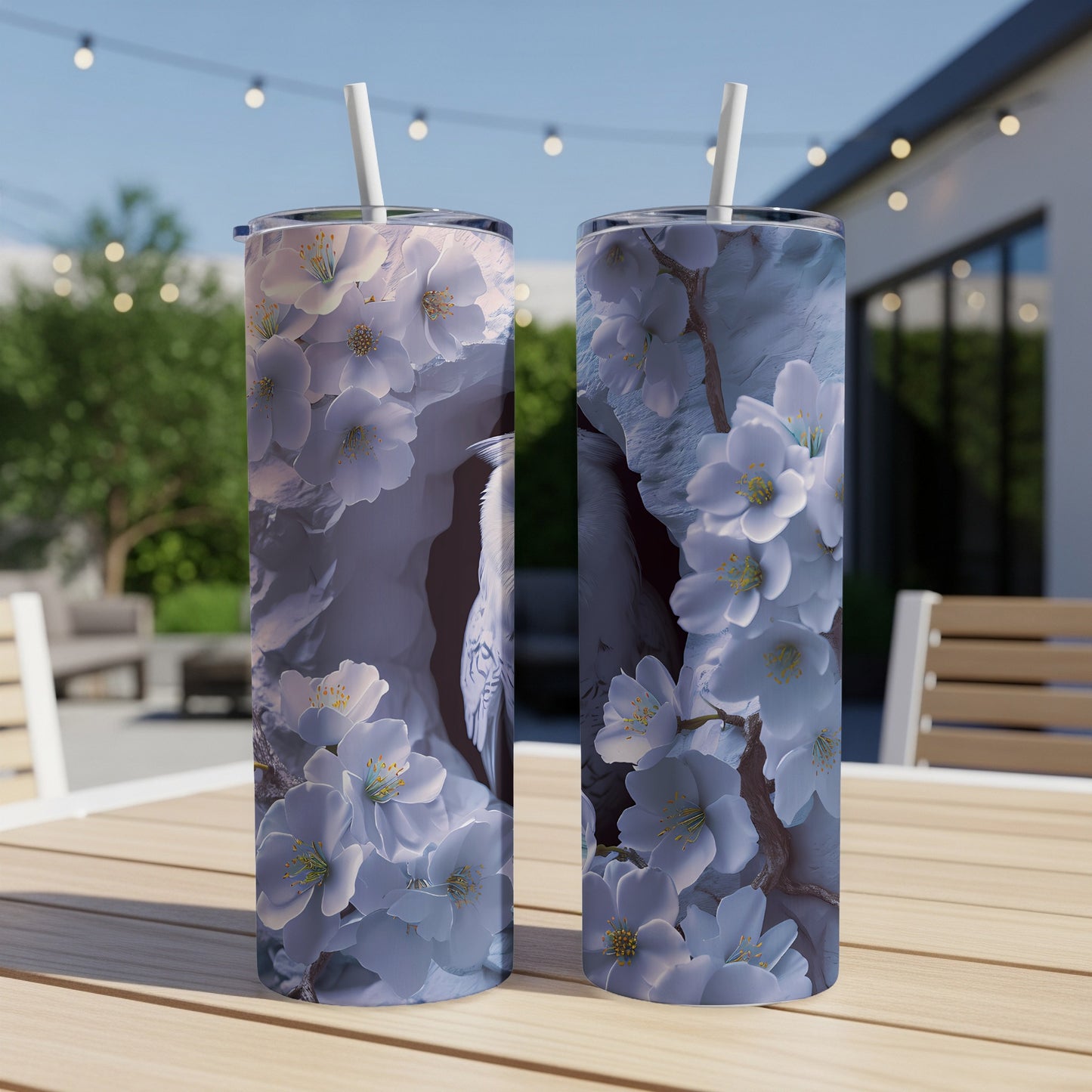 Two white ceramic tumblers with white straws, adorned with a blue and white bird and floral design.