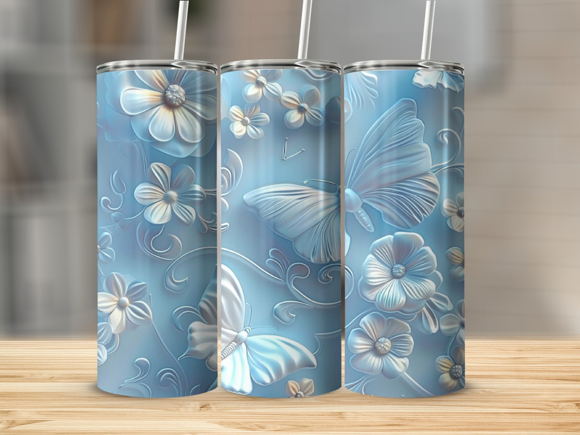 Three light blue tumblers with raised floral and butterfly designs on a wooden surface.