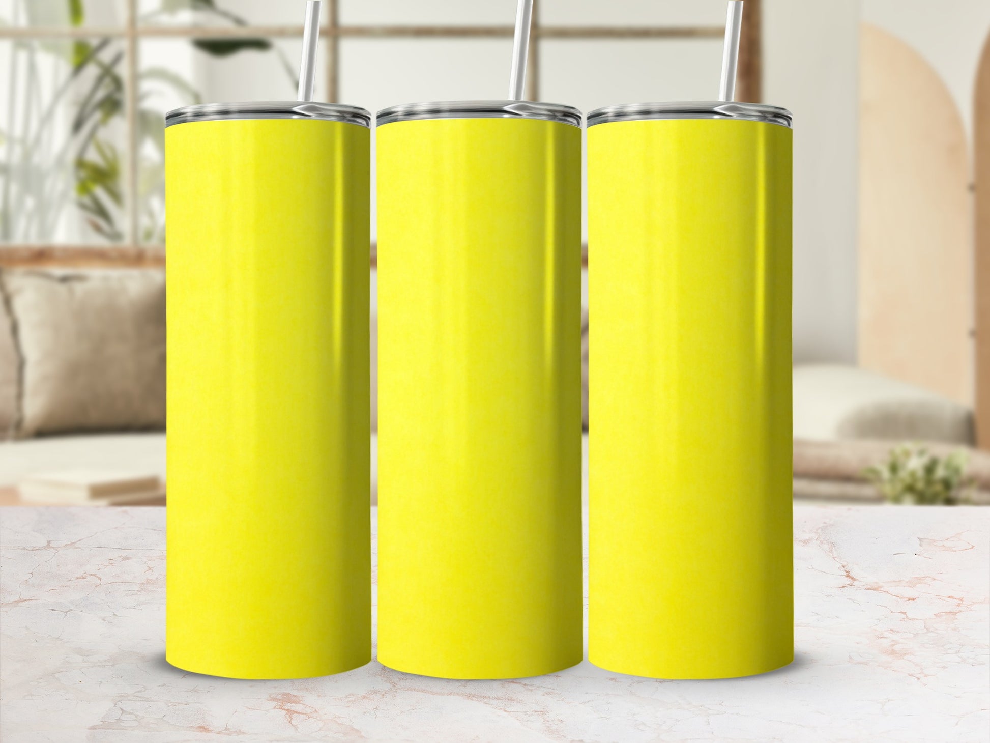 Three blank yellow tumblers with straws sit side-by-side on a marble surface.