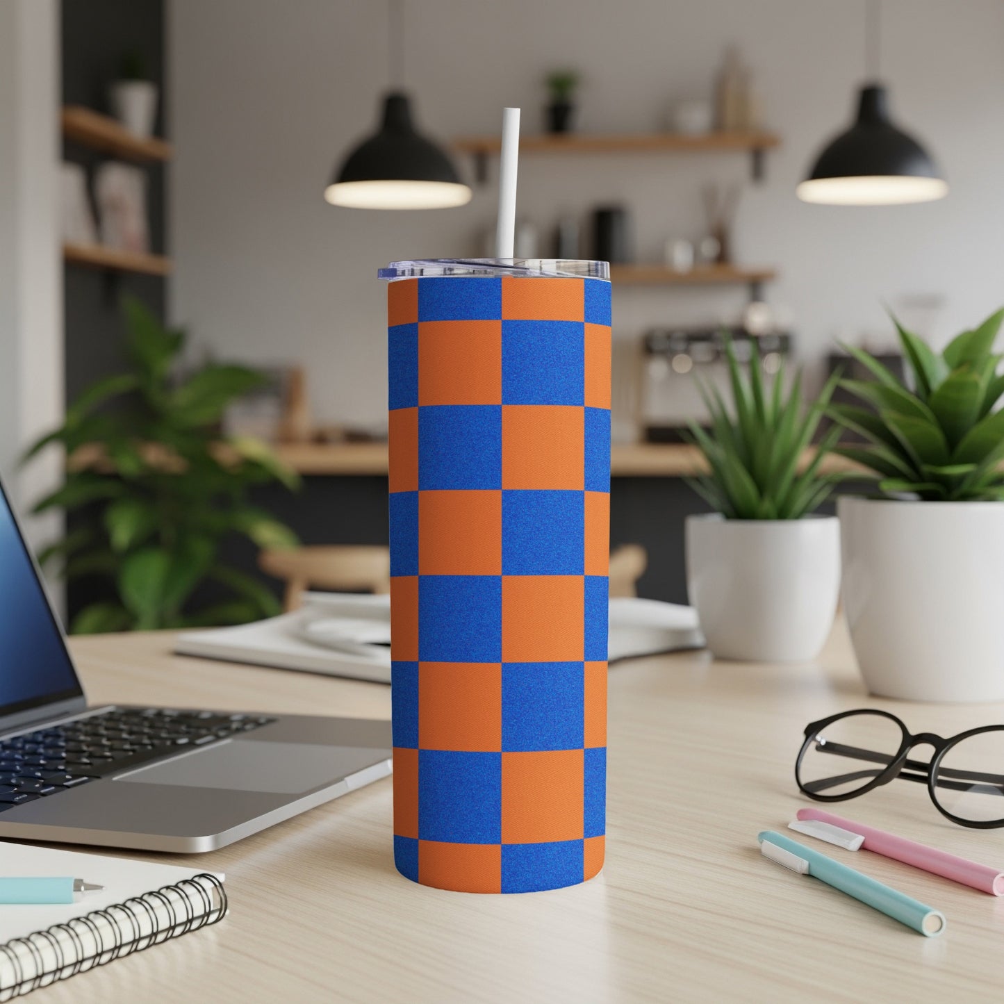 Orange and blue checkered tumbler with a white straw on a desk.