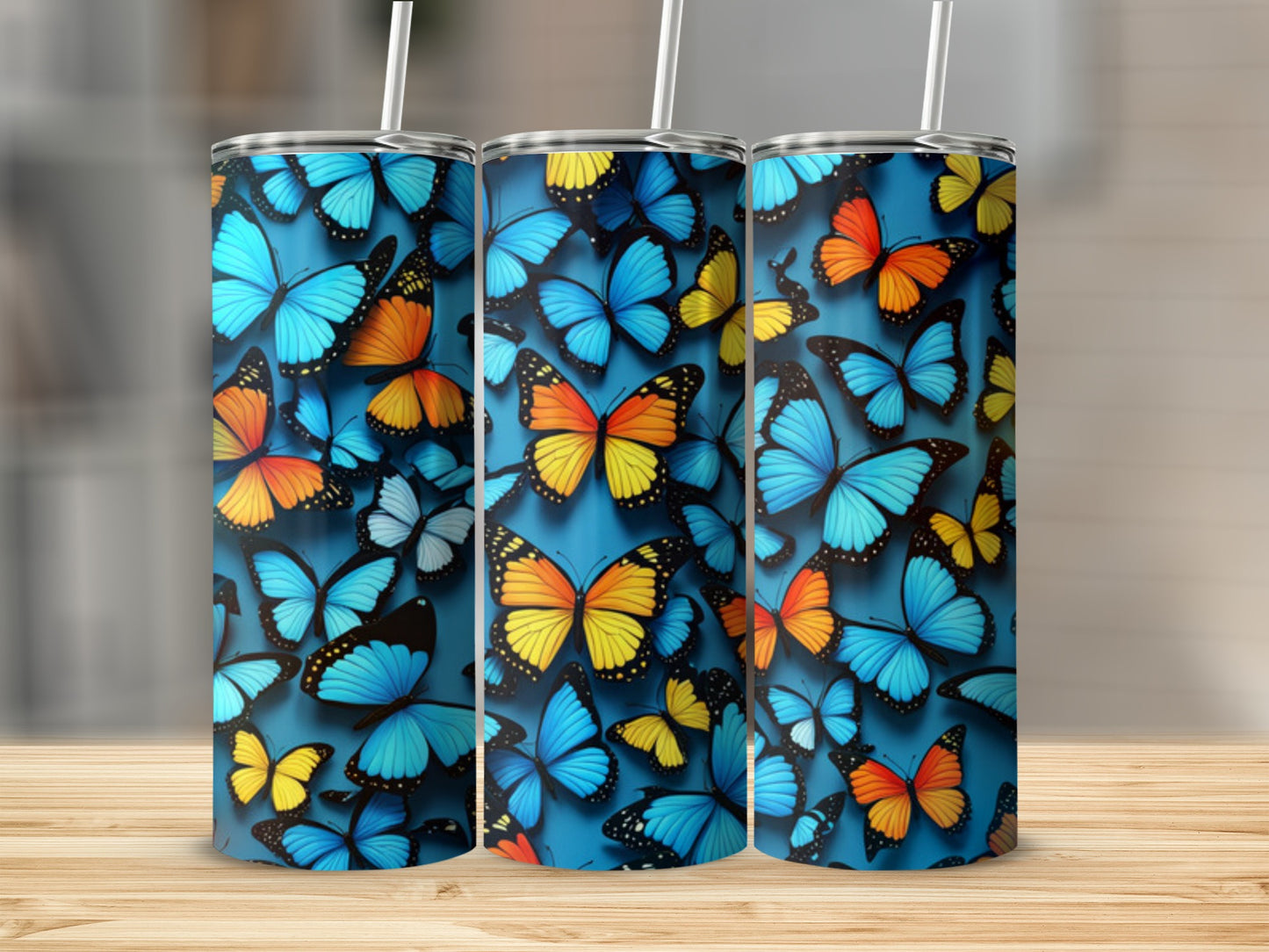 Three blue tumblers adorned with colorful butterflies, set on a wooden surface.