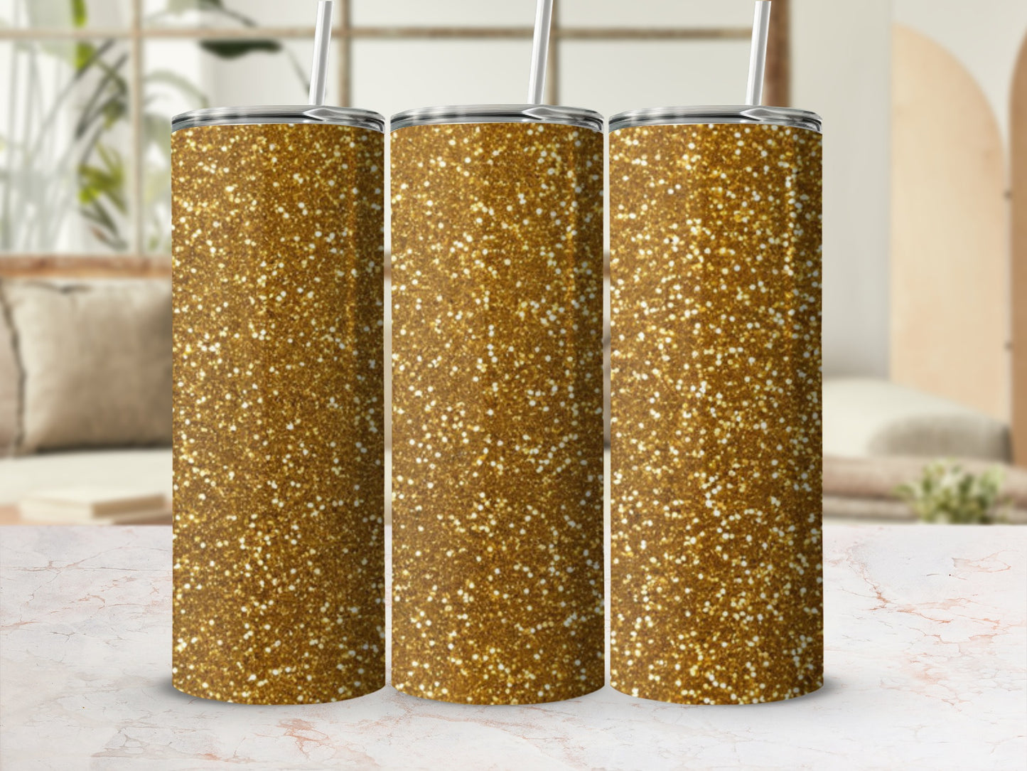 Three glitter gold tumblers with straws on a marbled surface.