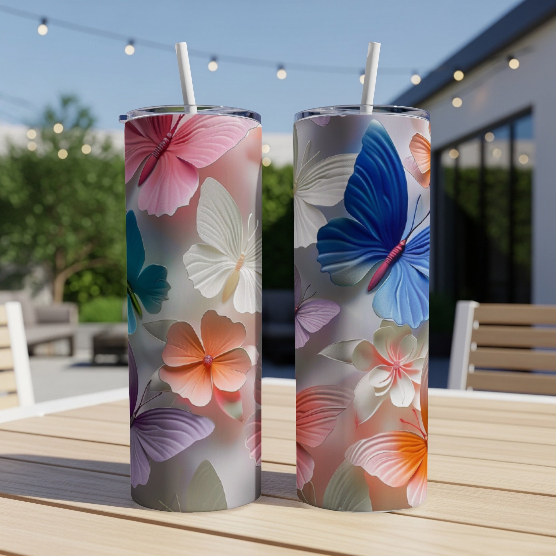 Two tumblers with a butterfly and floral pattern on a table outdoors.