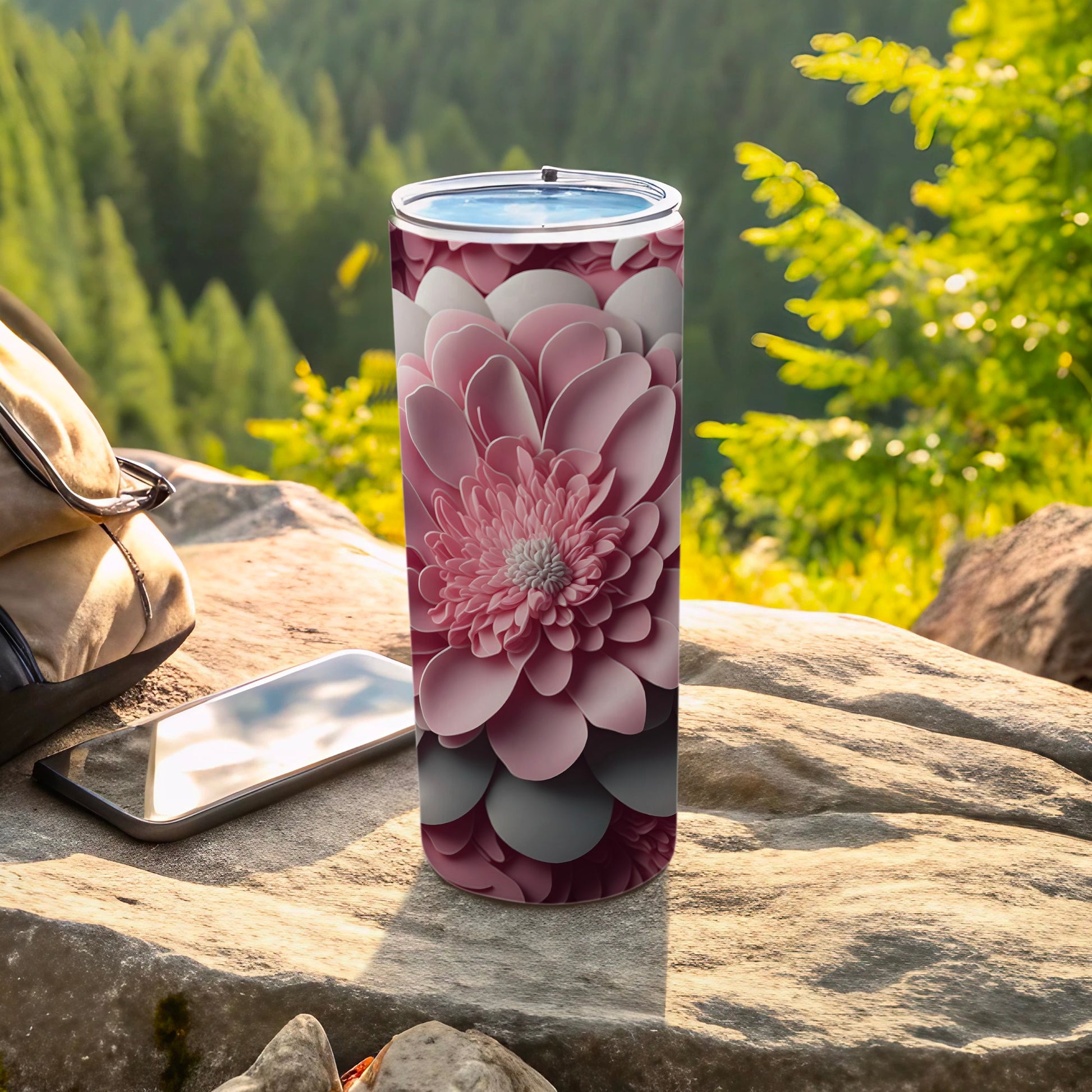 Pink floral patterned tumbler on rock with phone and backpack.