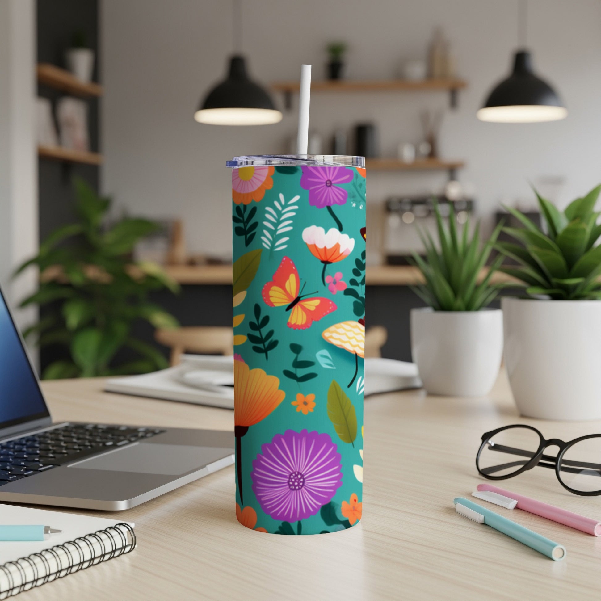 Teal tumbler with colorful floral and butterfly pattern on a desk.