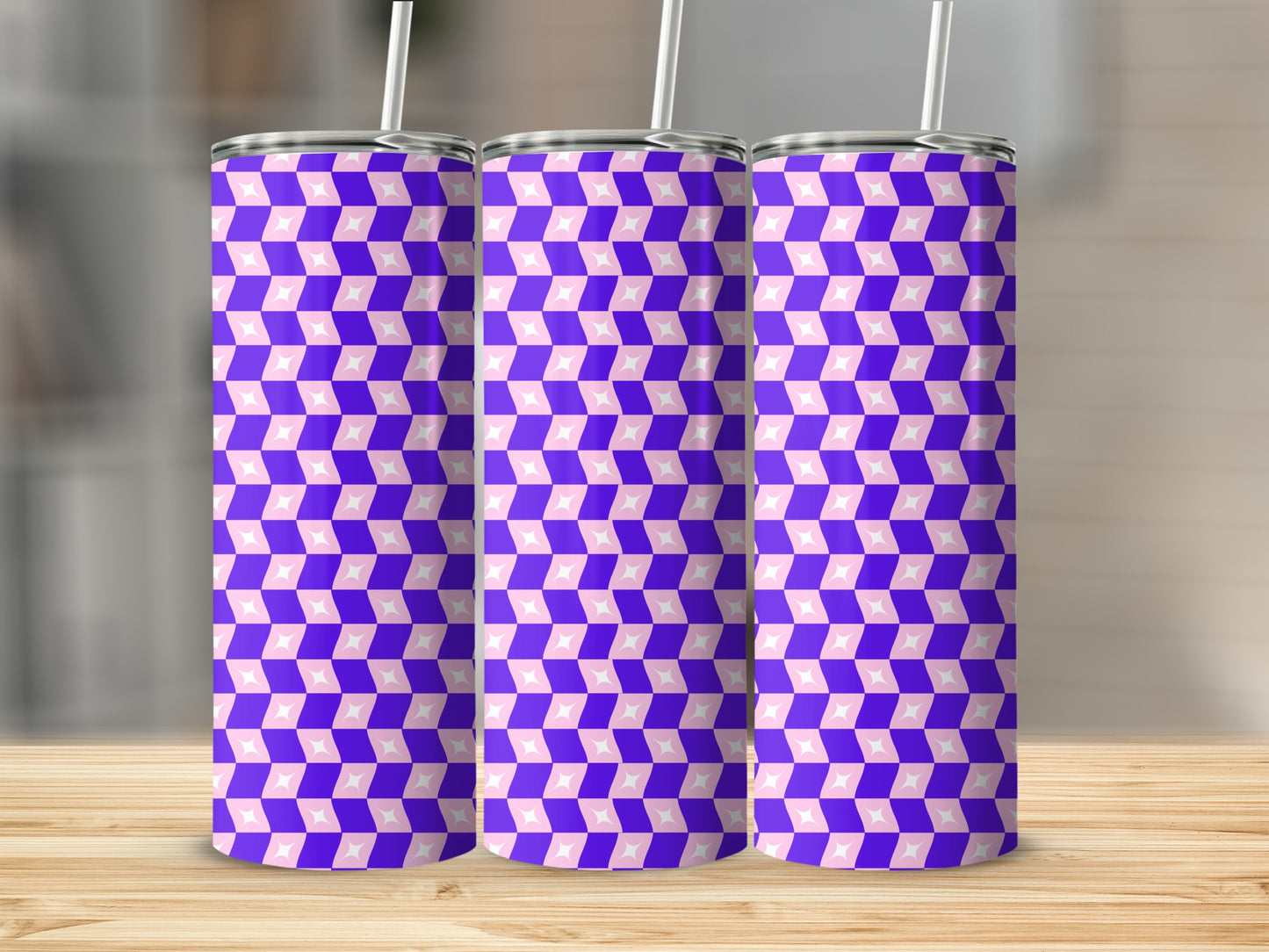 Three purple and pink geometric patterned tumblers with straws on a wooden surface.