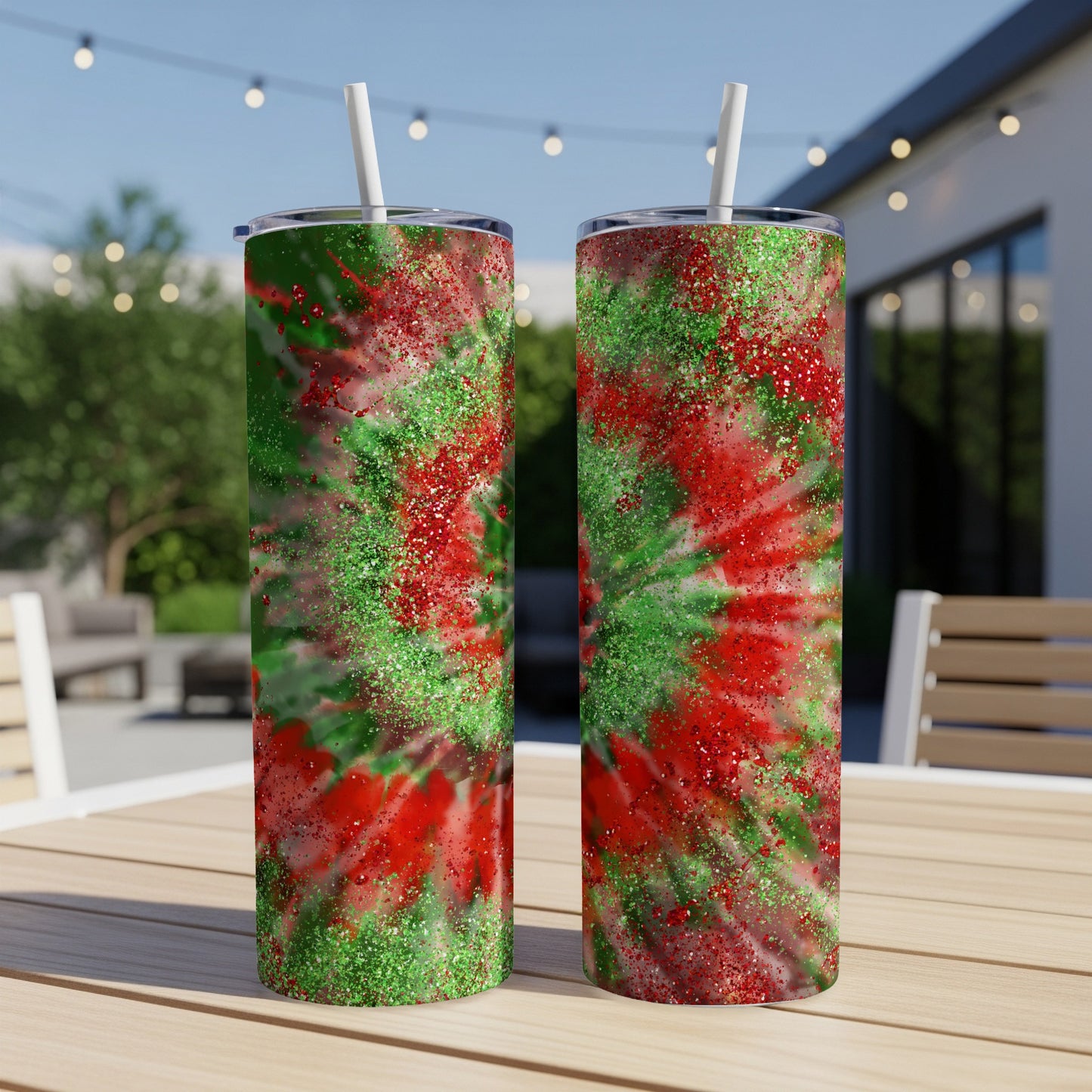 Two glittery red and green tie-dye tumblers with straws on a wooden table.