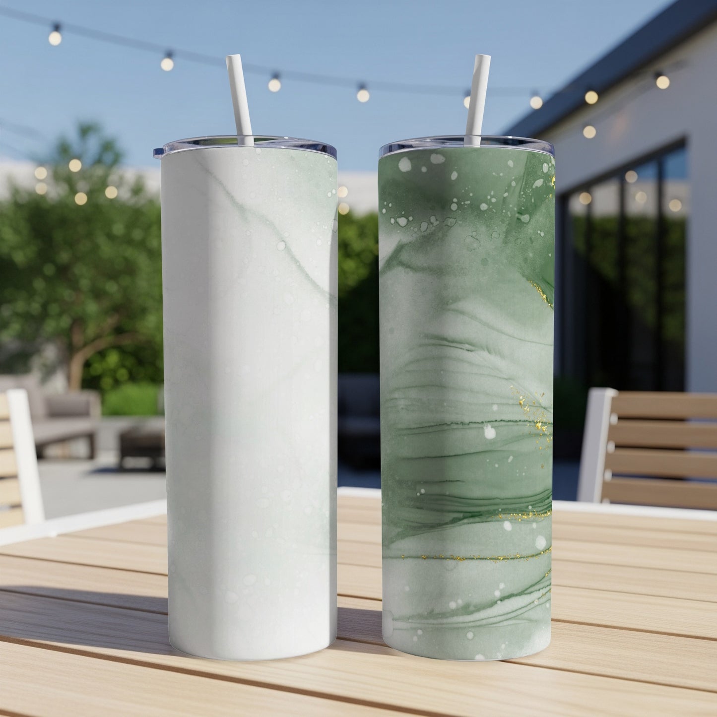 Two abstract patterned tumblers with straws on a wooden table outdoors.