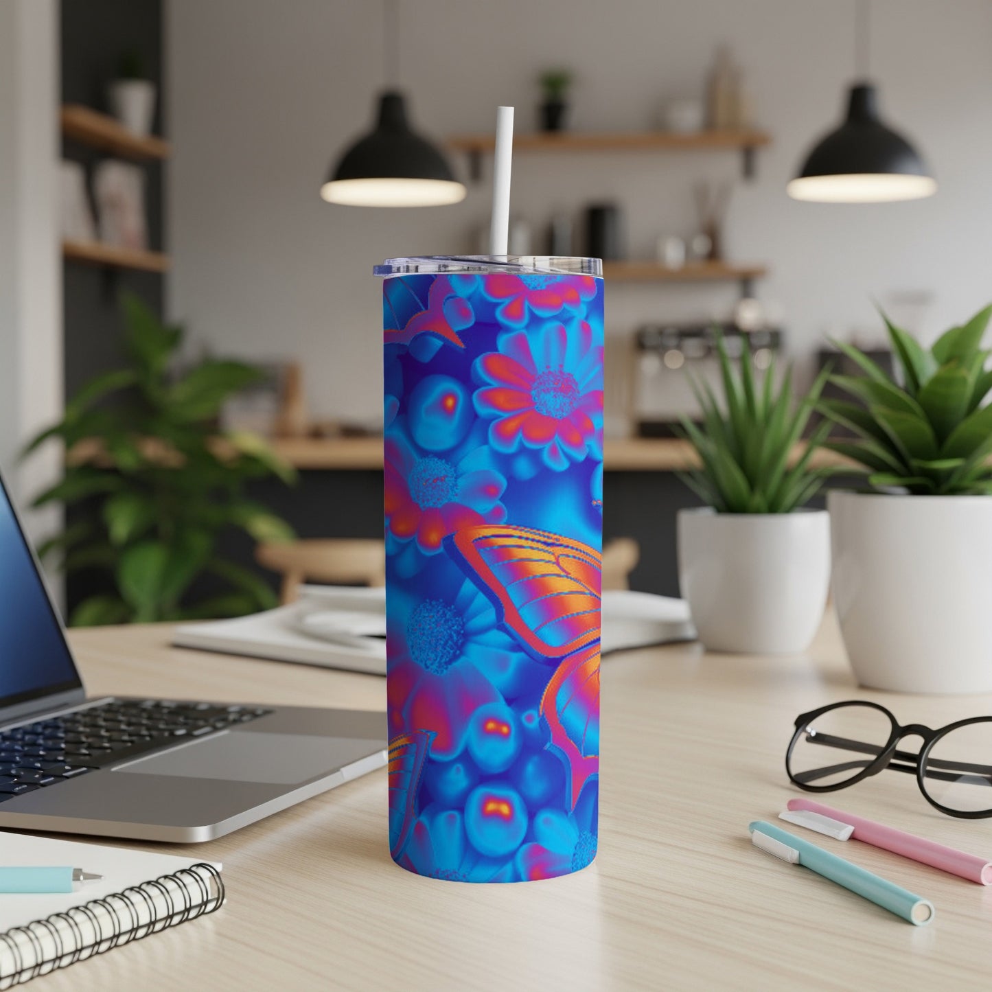 Blue tumbler with butterfly and floral design, with straw, on a desk.