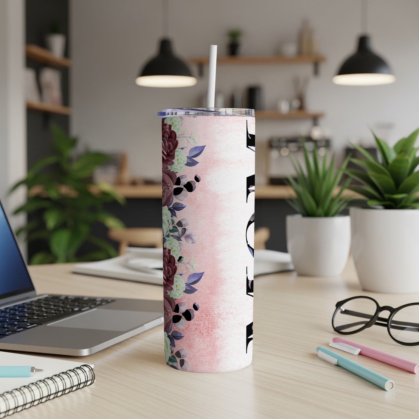 Pink floral tumbler with white lid and straw on a desk.