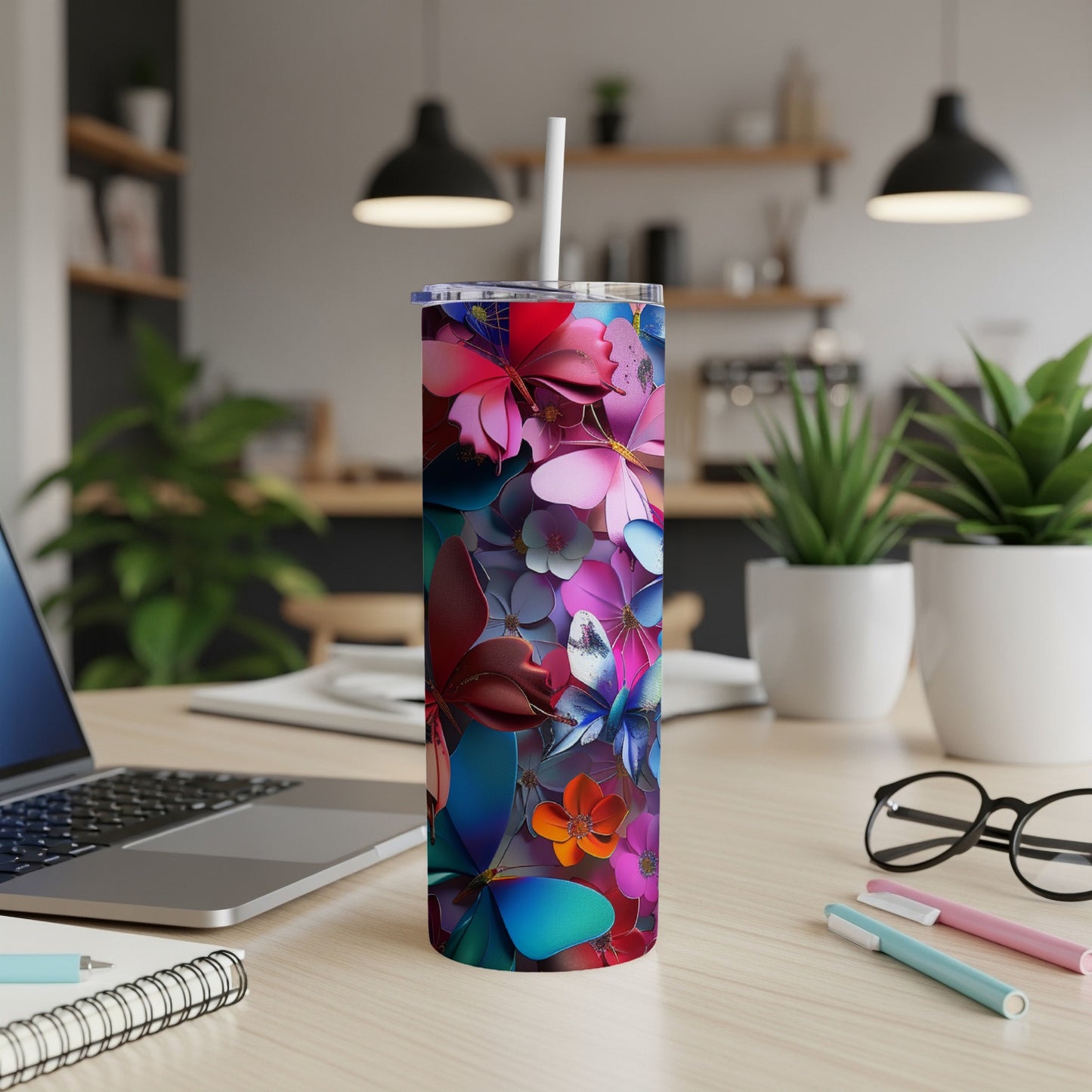Pink, blue, and red floral tumbler with straw on a desk.