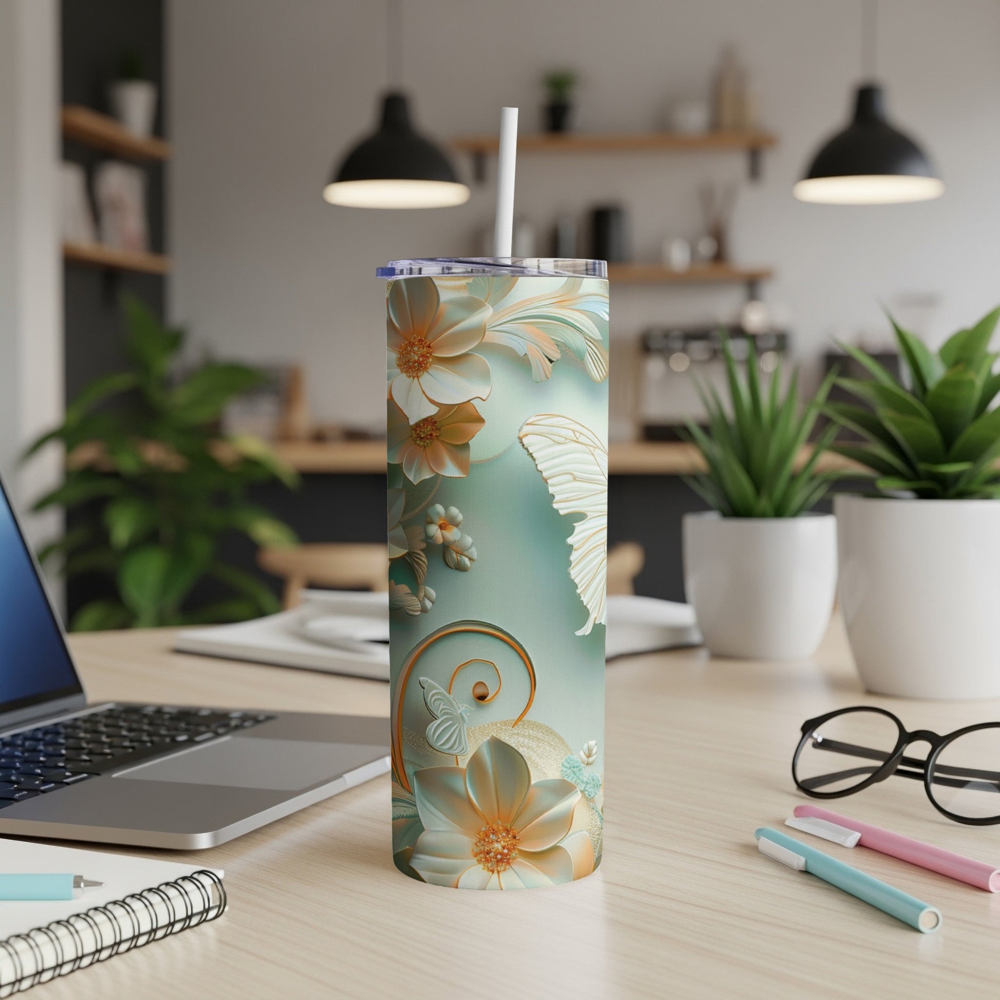 Floral and butterfly design on a mint green tumbler with a straw, on a desk.
