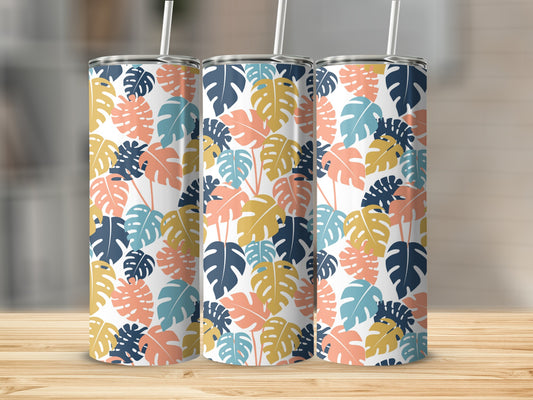 Three tropical leaf patterned tumblers with straws on a wooden surface.
