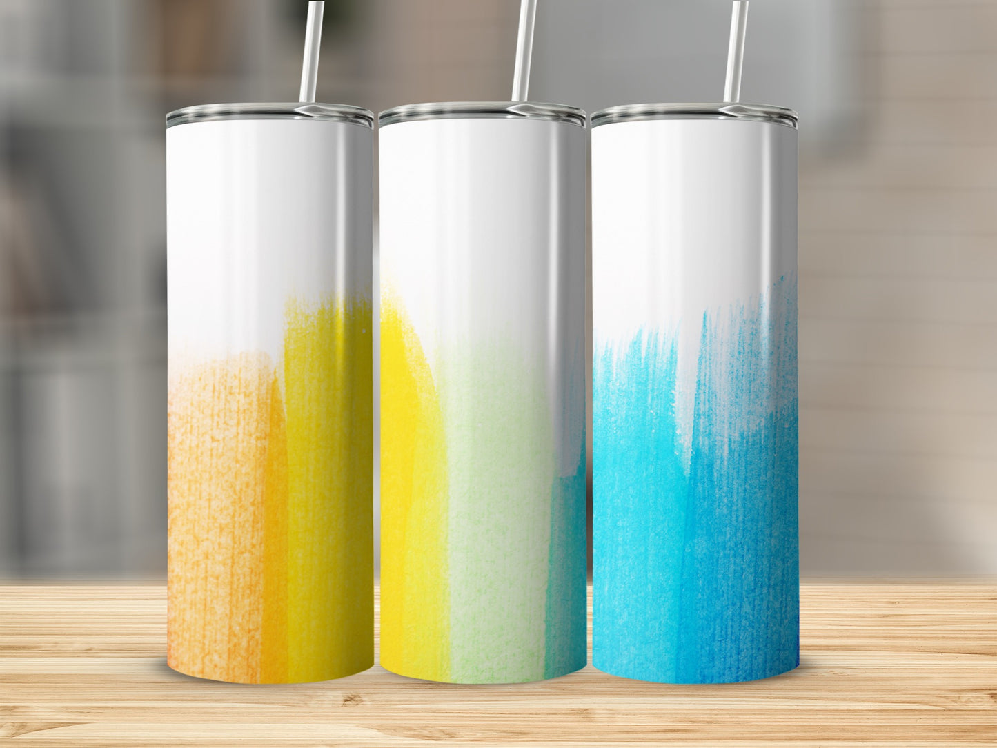 Three stainless steel tumblers with colorful painted designs: orange, yellow, and blue.