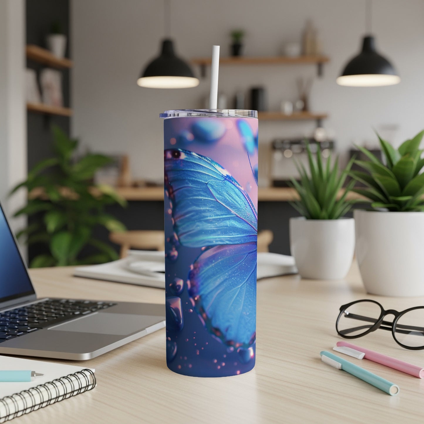 Blue butterfly tumbler with straw on a desk next to a laptop.