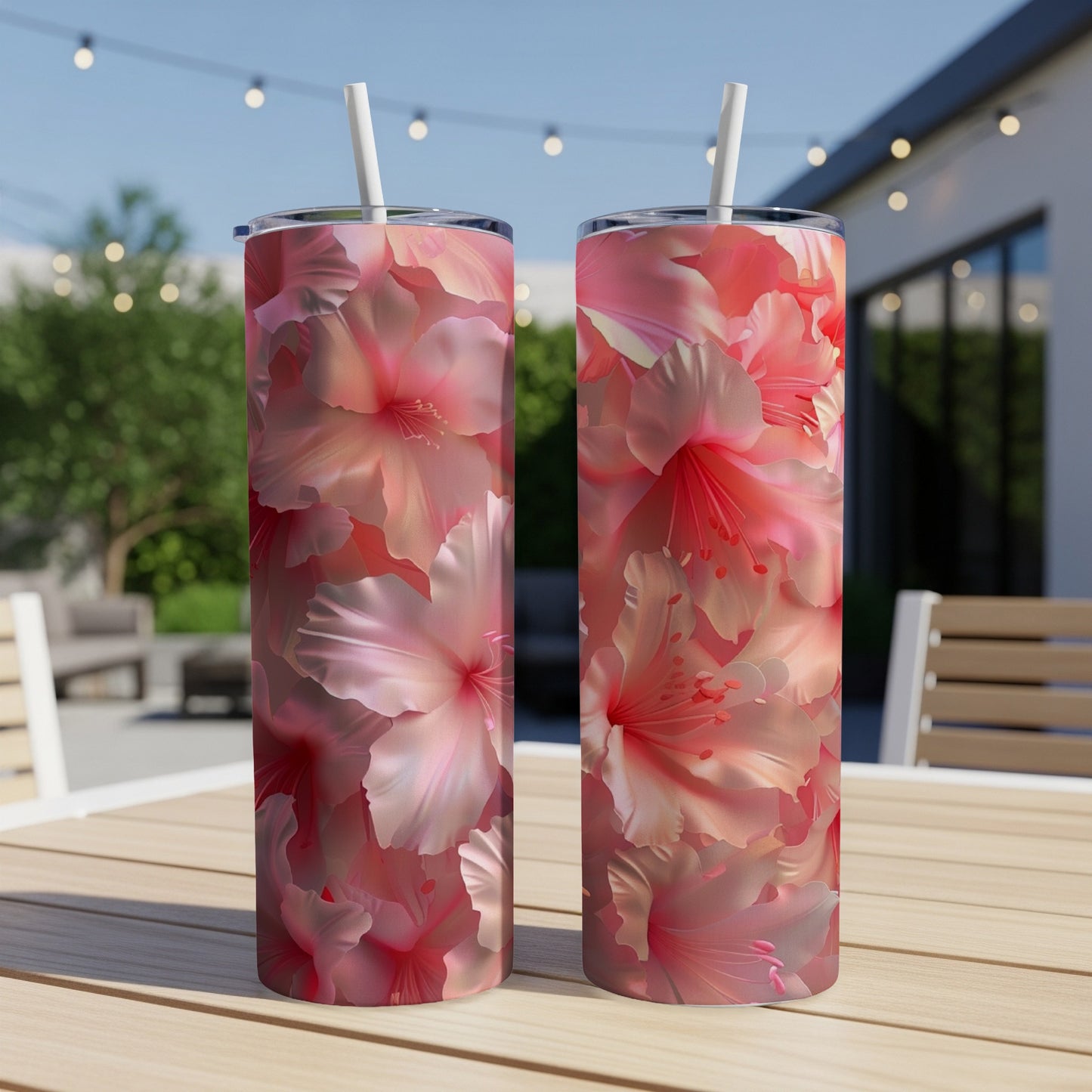 Two tumblers with a vibrant pink hibiscus floral pattern sit on a wooden table outdoors.