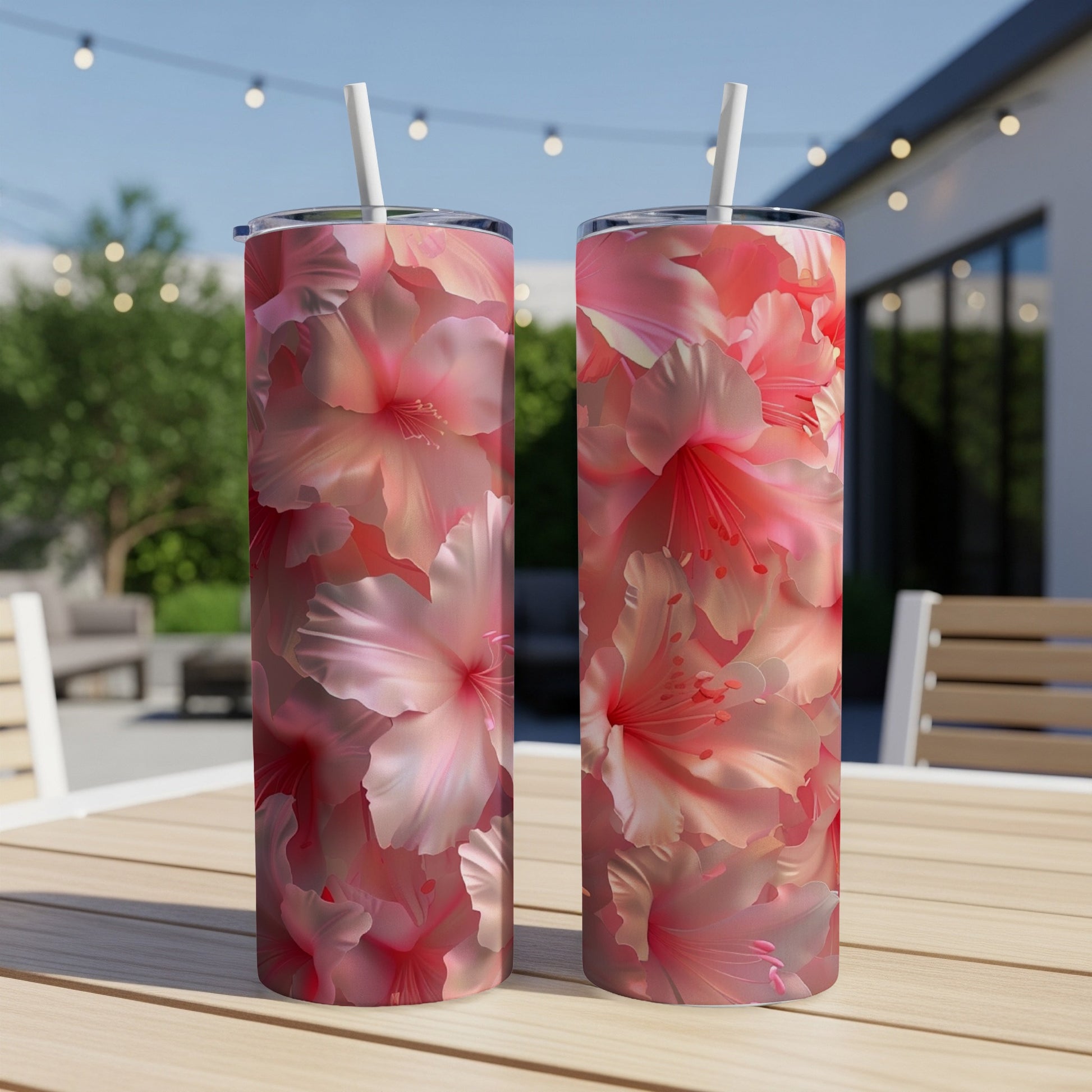 Two tumblers with a vibrant pink hibiscus floral pattern sit on a wooden table outdoors.