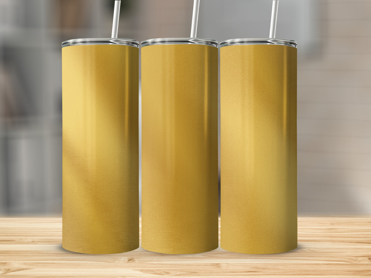 Three gold tumblers with straws stand on a wooden surface.