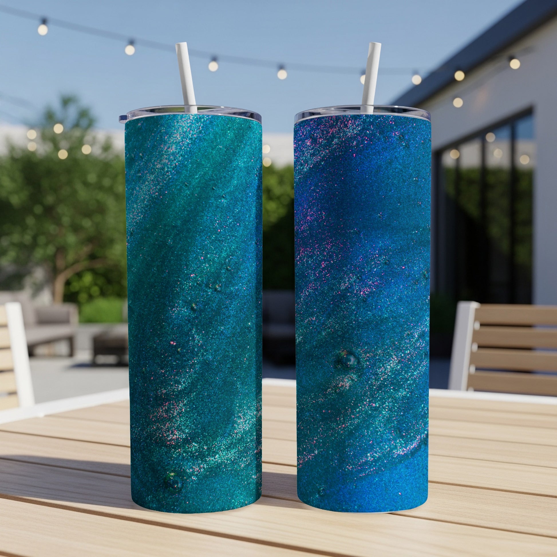 Two glittery blue and teal tumblers with straws on an outdoor table.